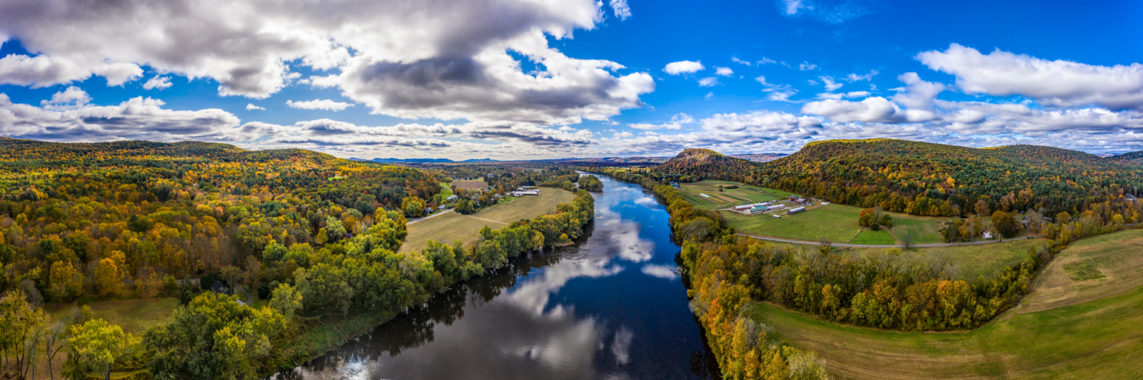 Picture of river reflecting blue sky cutting through farm and fall colored trees