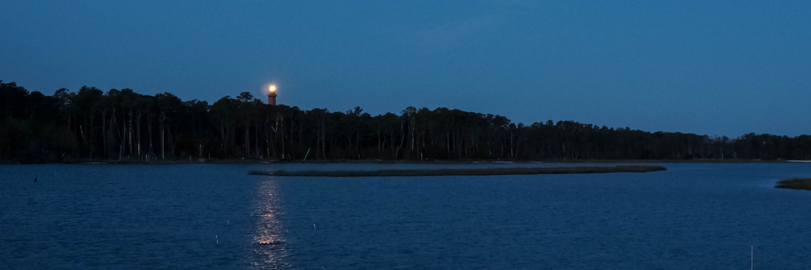 Atlantic Ocean at dusk with lighthouse rising above darkened trees.