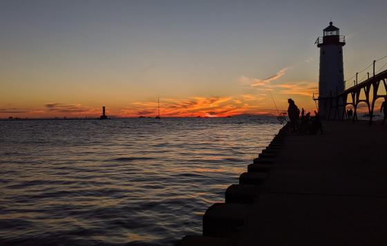 Wave break, lighthouse, and people fishing silhoueted with Lake Michigan at sunset. Credit: Jennifer Schlicht 