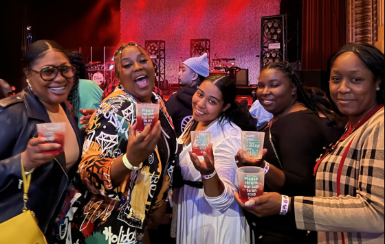 Reusable cup sign at music venue and group of attendees posing with their cups